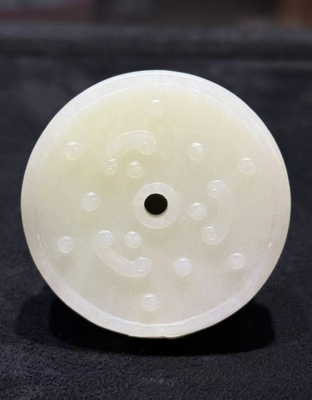 Pixiu jade pendant hand-carved from creamy white nephrite as a thick round disc with two coiled pixiu carved on the top surface and a small central hole