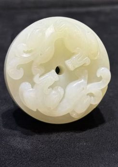 Pixiu jade pendant hand-carved from creamy white nephrite as a thick round disc with two coiled pixiu carved on the top surface and a small central hole