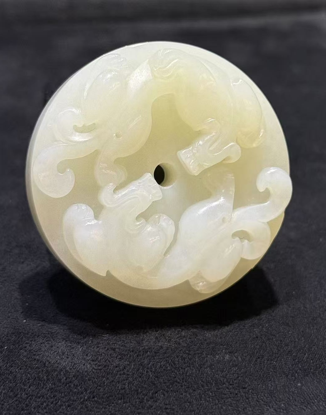 Pixiu jade pendant hand-carved from creamy white nephrite as a thick round disc with two coiled pixiu carved on the top surface and a small central hole