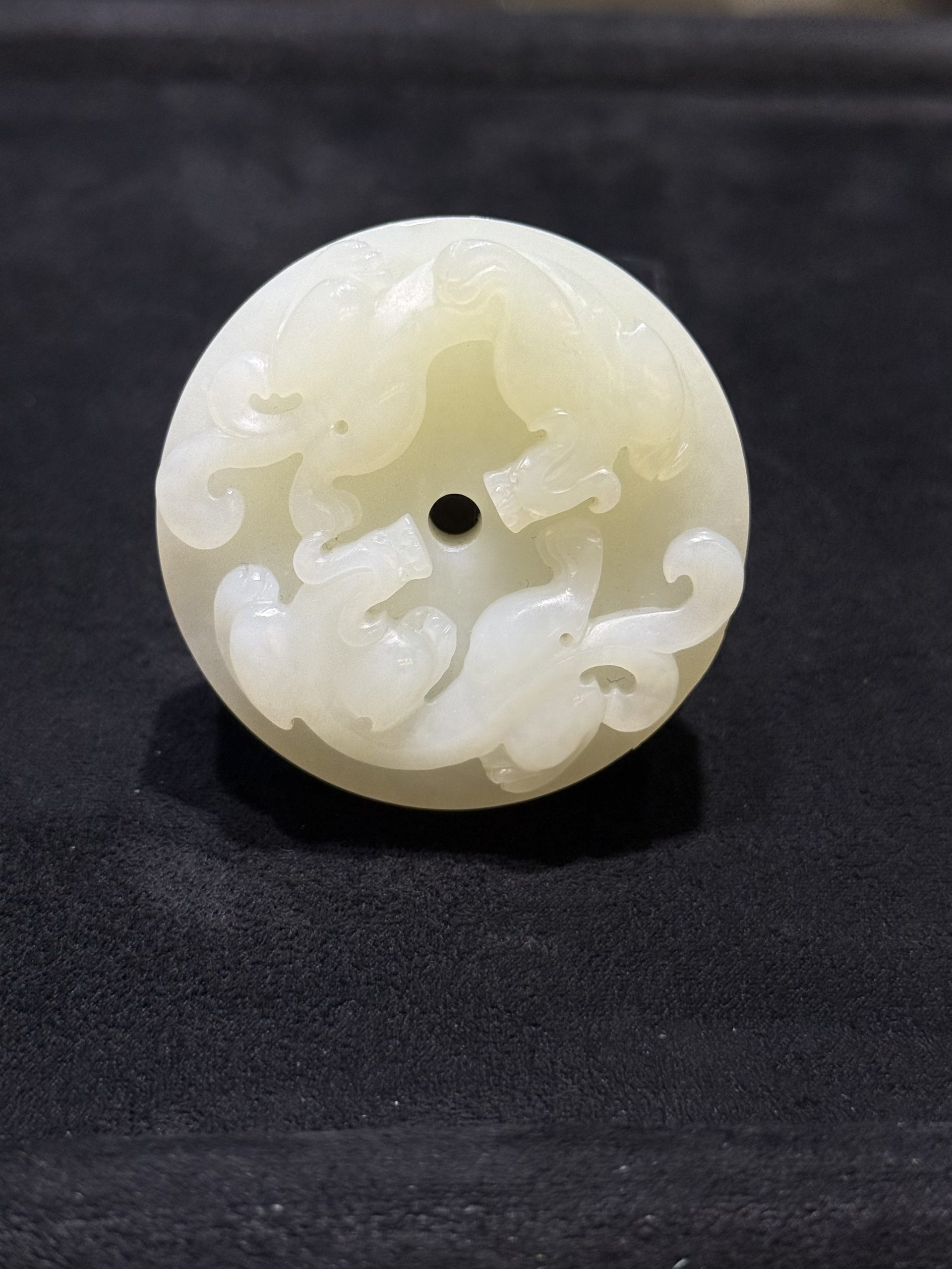 Pixiu jade pendant hand-carved from creamy white nephrite as a thick round disc with two coiled pixiu carved on the top surface and a small central hole
