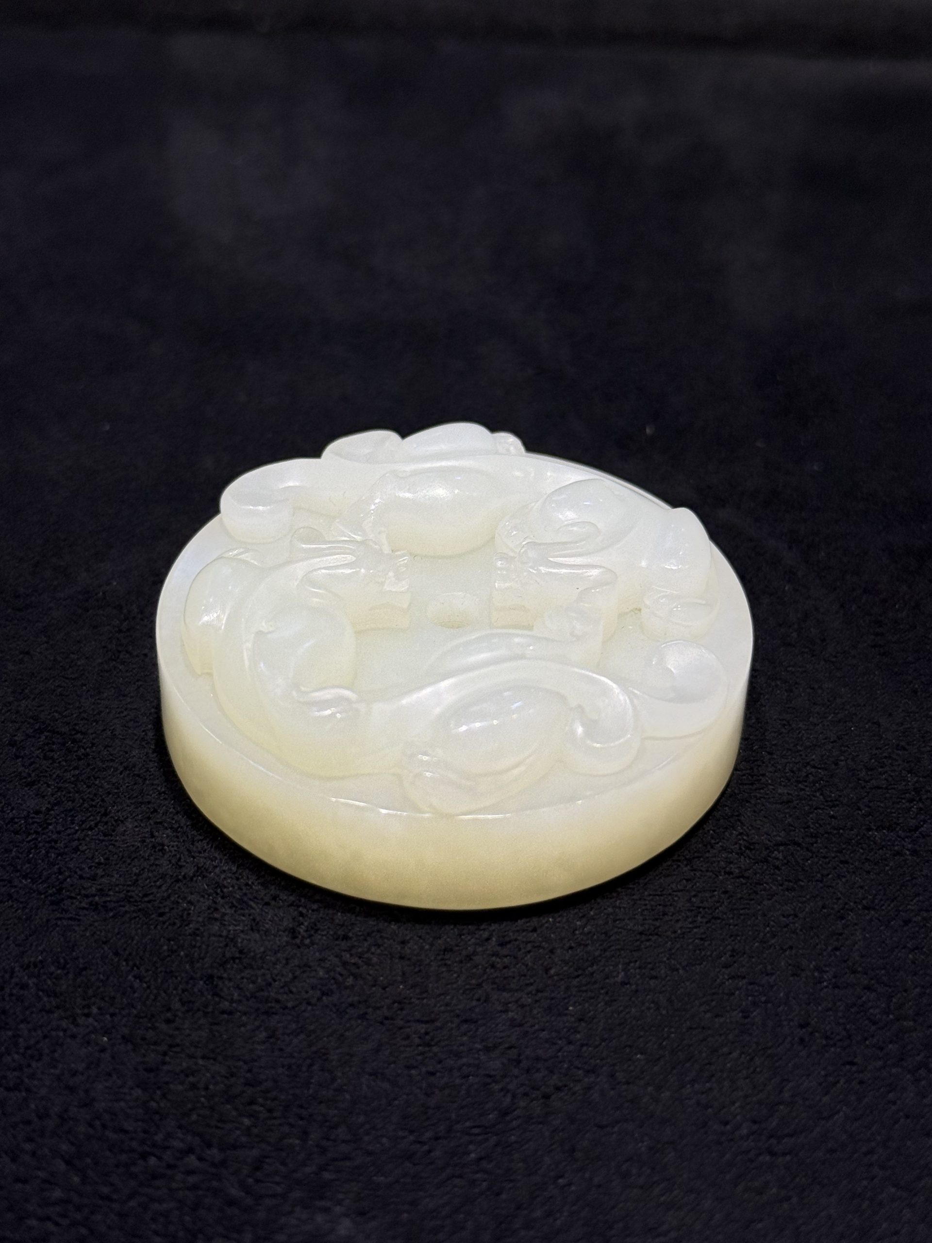 Pixiu jade pendant hand-carved from creamy white nephrite as a thick round disc with two coiled pixiu carved on the top surface and a small central hole