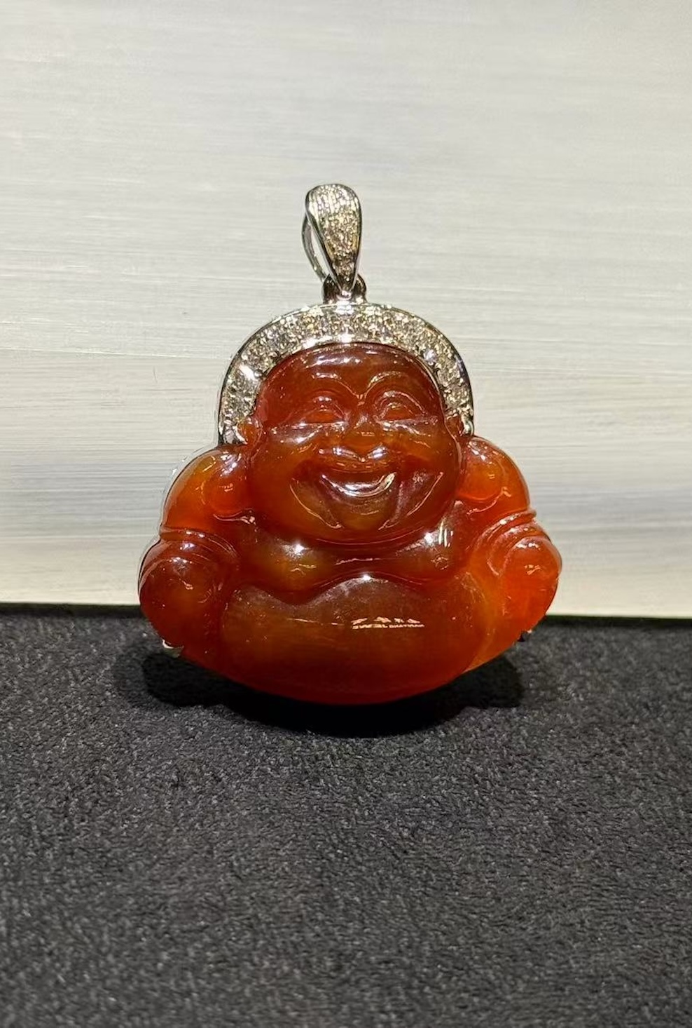 Laughing buddha jade pendant carved from translucent brownish red jadeite showing a smiling Buddha with a round belly, set in an 18k white gold bail with small diamonds