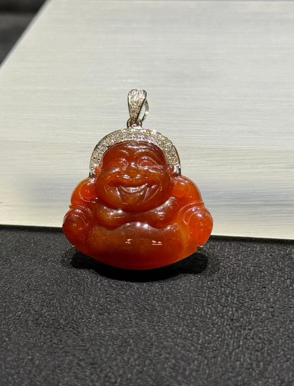 Laughing buddha jade pendant carved from translucent brownish red jadeite showing a smiling Buddha with a round belly, set in an 18k white gold bail with small diamonds