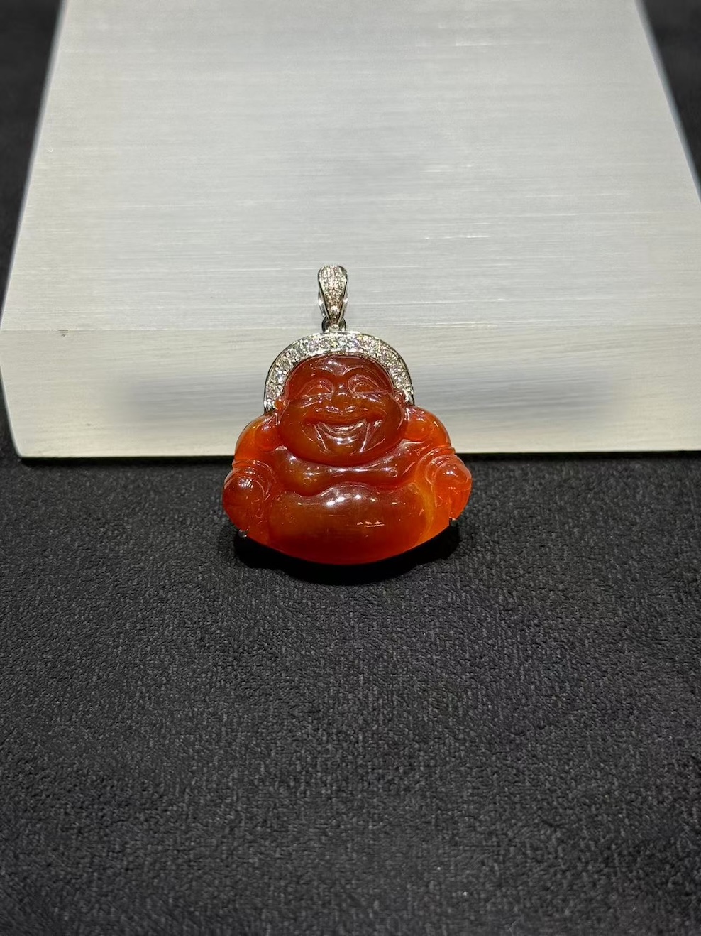 Laughing buddha jade pendant carved from translucent brownish red jadeite showing a smiling Buddha with a round belly, set in an 18k white gold bail with small diamonds