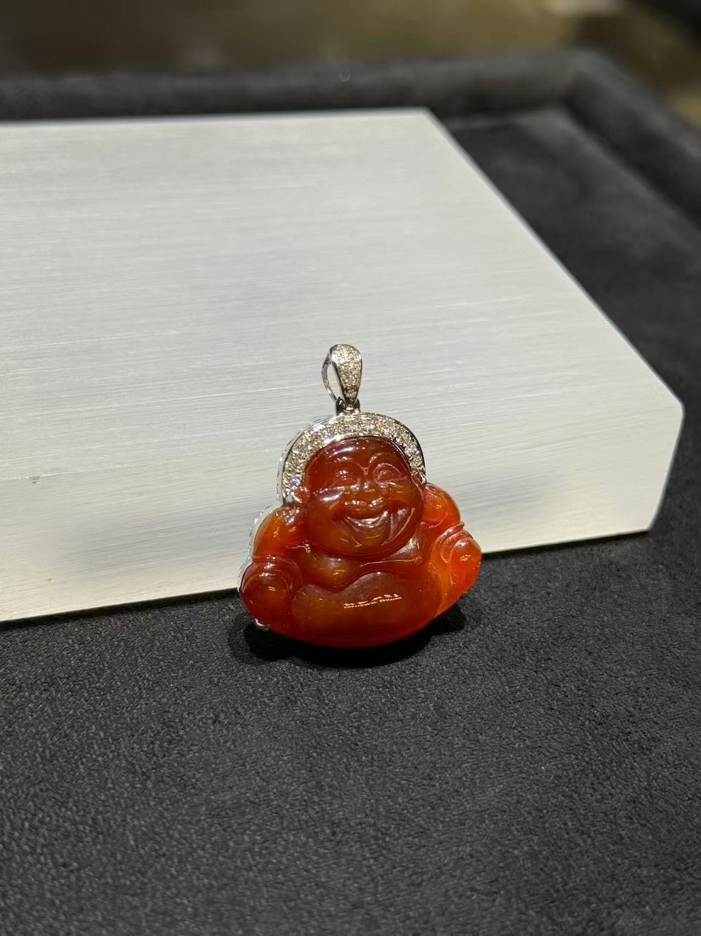 Laughing buddha jade pendant carved from translucent brownish red jadeite showing a smiling Buddha with a round belly, set in an 18k white gold bail with small diamonds