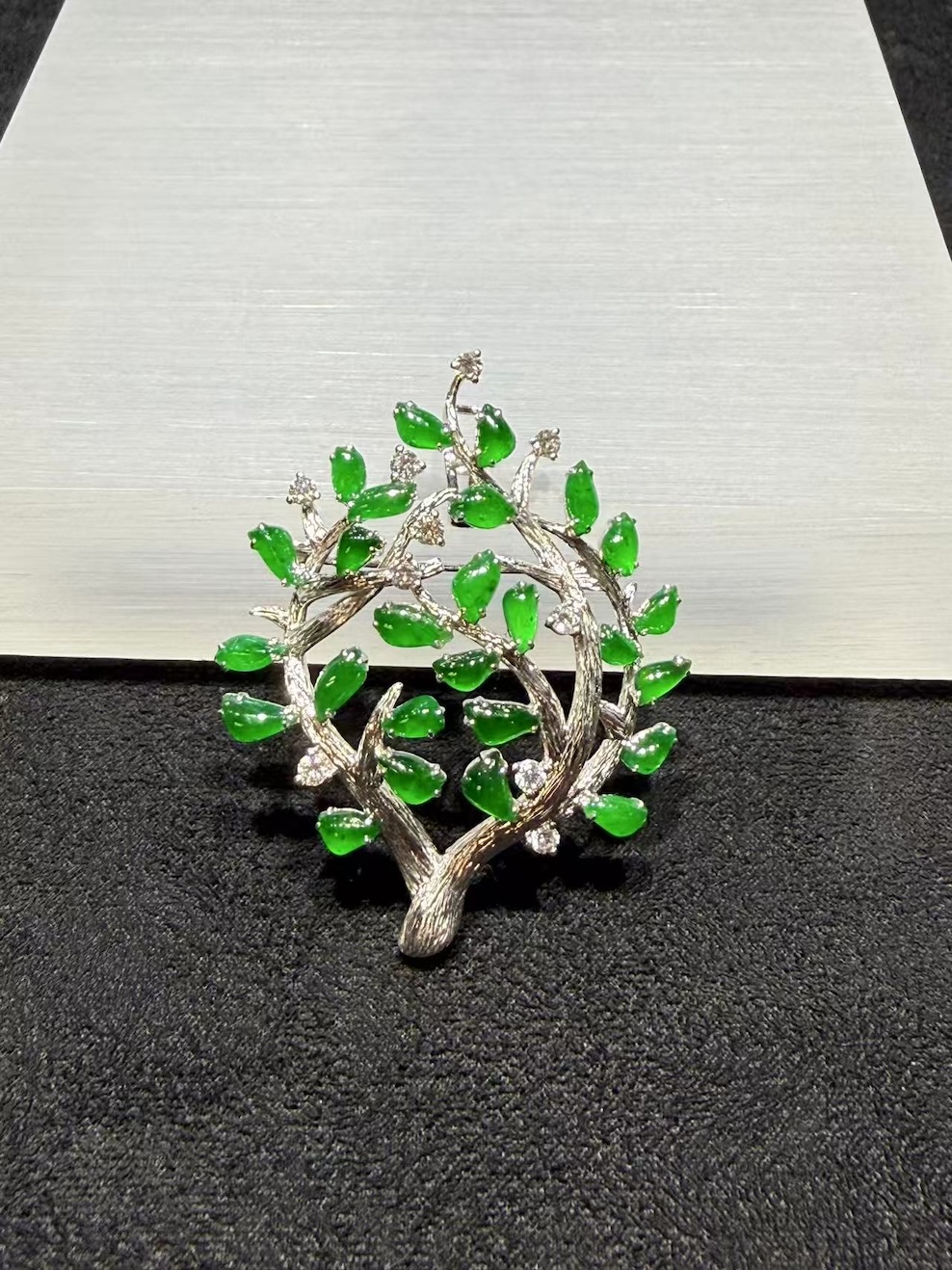 Jade tree brooch pendant with highly translucent vibrant green jadeite leaves on textured 18k white gold branches, set with small diamond accents, designed as a longevity tree