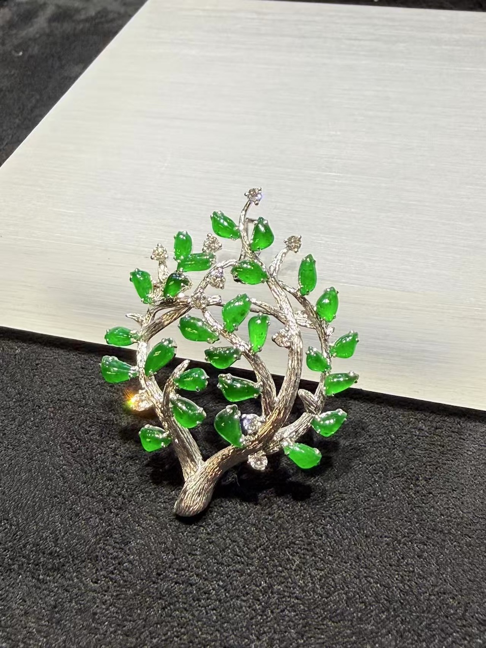 Jade tree brooch pendant with highly translucent vibrant green jadeite leaves on textured 18k white gold branches, set with small diamond accents, designed as a longevity tree