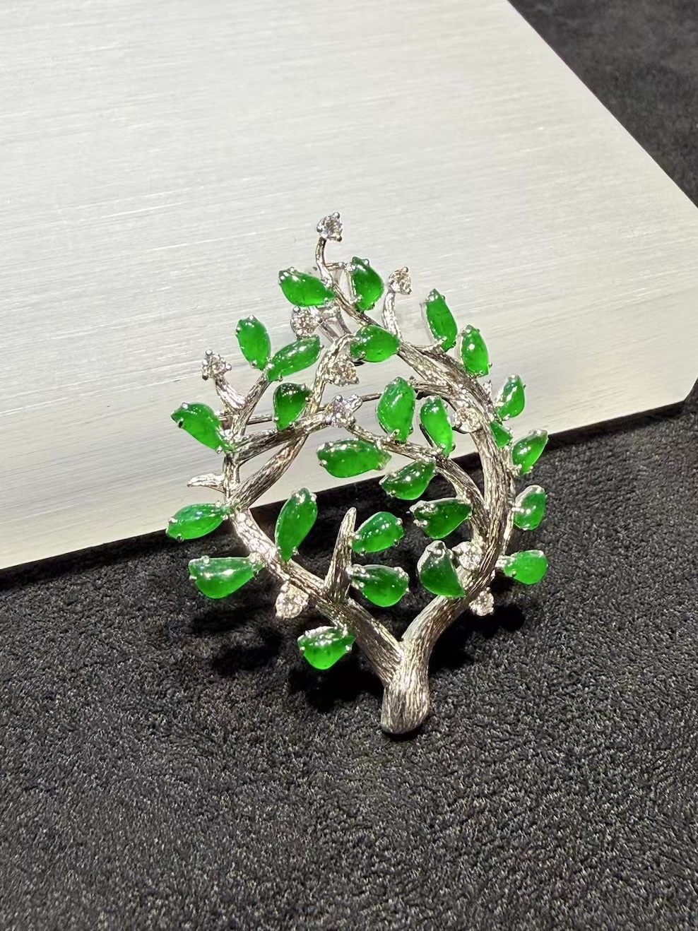 Jade tree brooch pendant with highly translucent vibrant green jadeite leaves on textured 18k white gold branches, set with small diamond accents, designed as a longevity tree