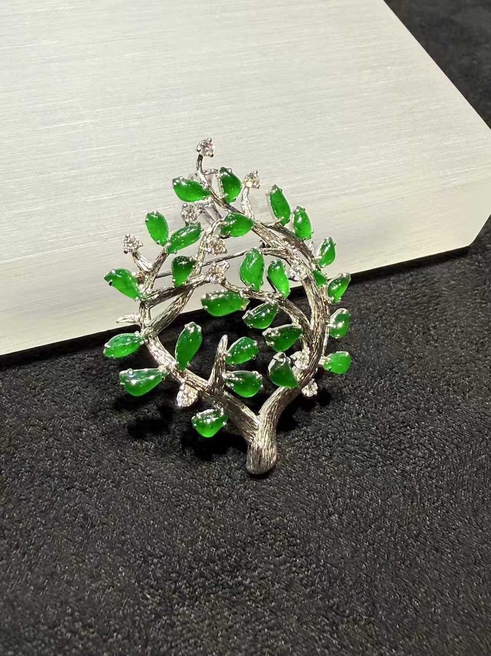 Jade tree brooch pendant with highly translucent vibrant green jadeite leaves on textured 18k white gold branches, set with small diamond accents, designed as a longevity tree