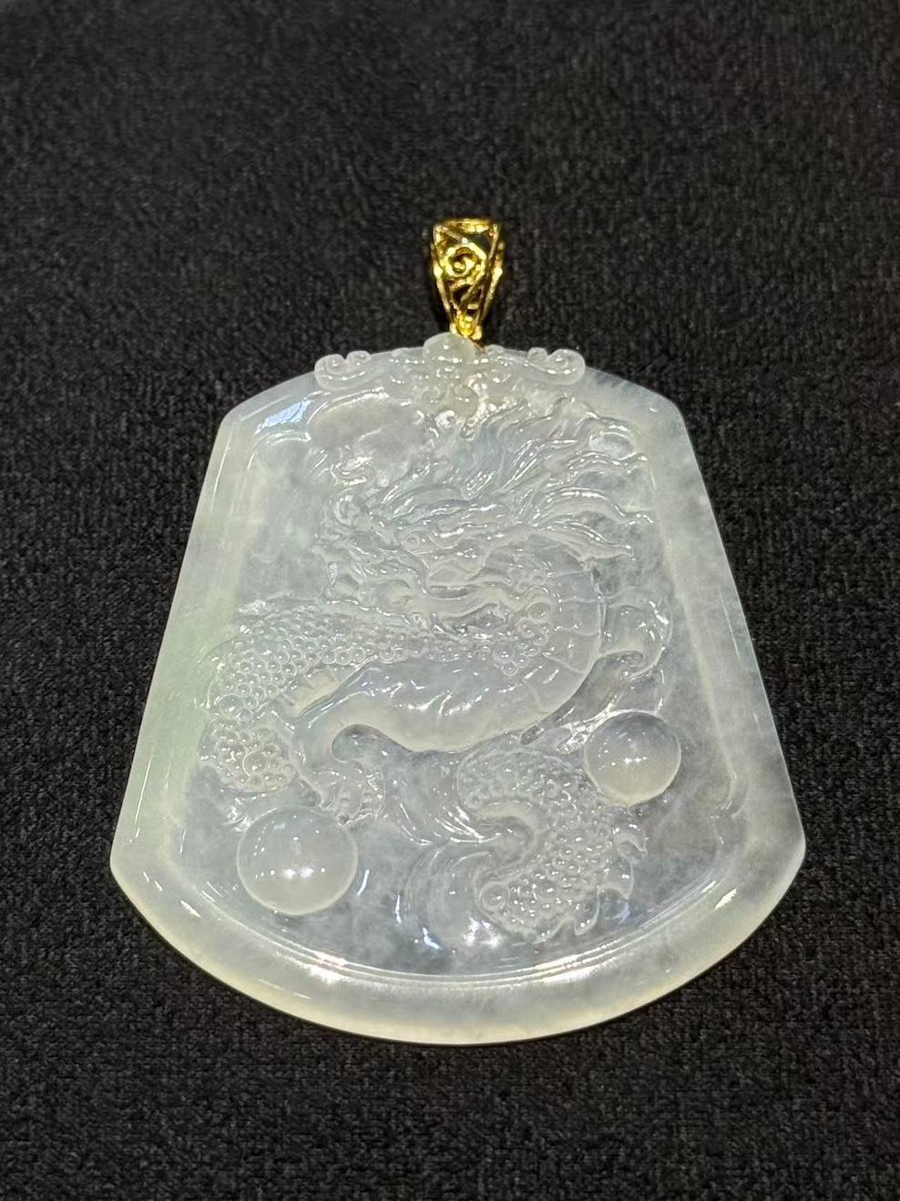 Dragon jade pendant hand-carved from icy translucent jadeite on a trapezoidal plaque, showing a dragon chasing a flaming pearl, finished with an 18k yellow gold bail