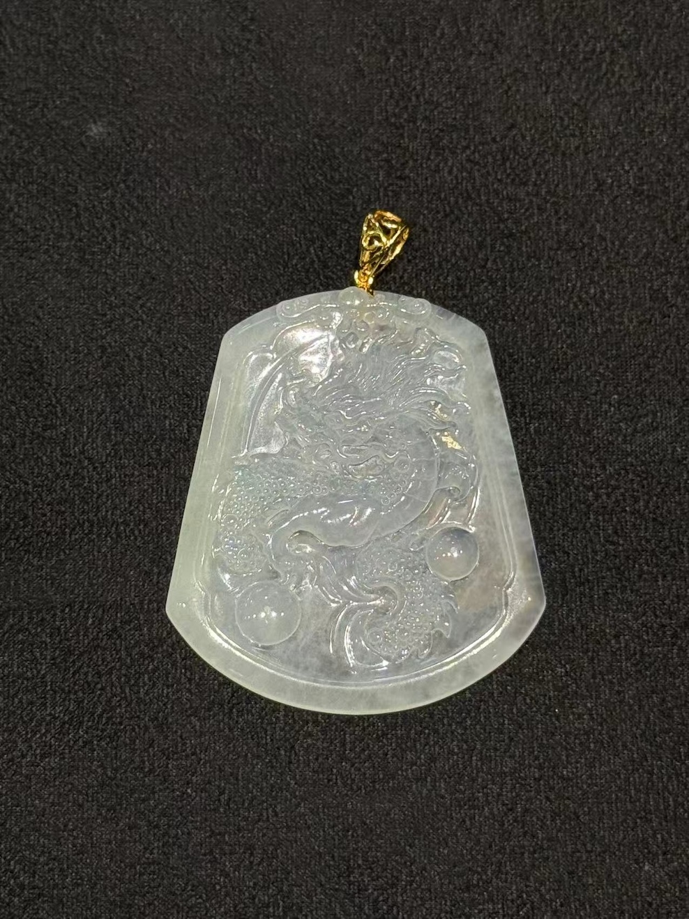 Dragon jade pendant hand-carved from icy translucent jadeite on a trapezoidal plaque, showing a dragon chasing a flaming pearl, finished with an 18k yellow gold bail