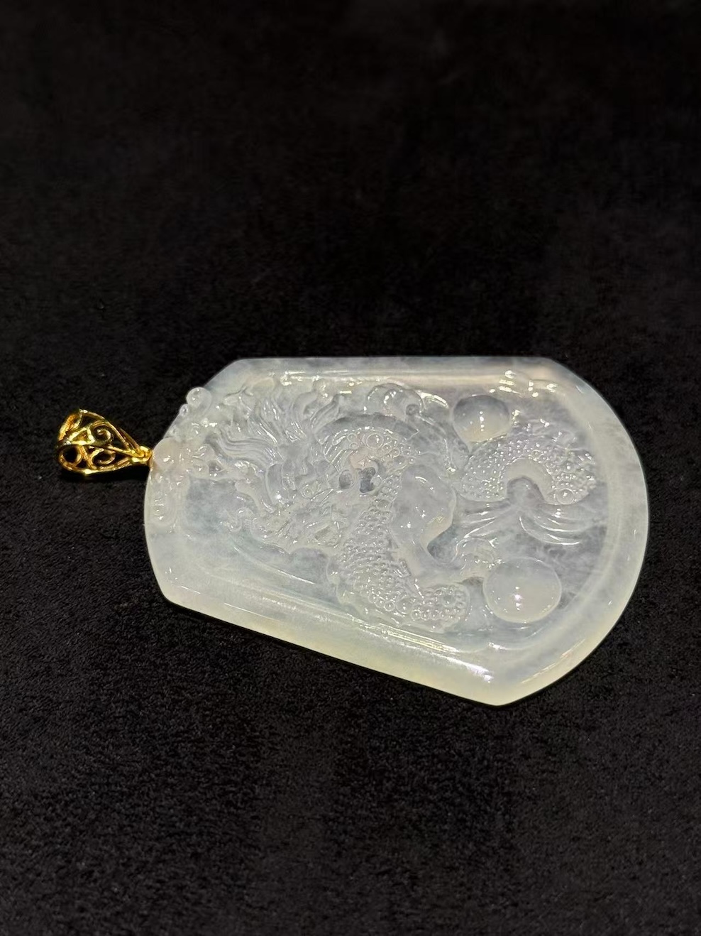 Dragon jade pendant hand-carved from icy translucent jadeite on a trapezoidal plaque, showing a dragon chasing a flaming pearl, finished with an 18k yellow gold bail