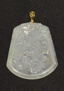 Dragon jade pendant hand-carved from icy translucent jadeite on a trapezoidal plaque, showing a dragon chasing a flaming pearl, finished with an 18k yellow gold bail