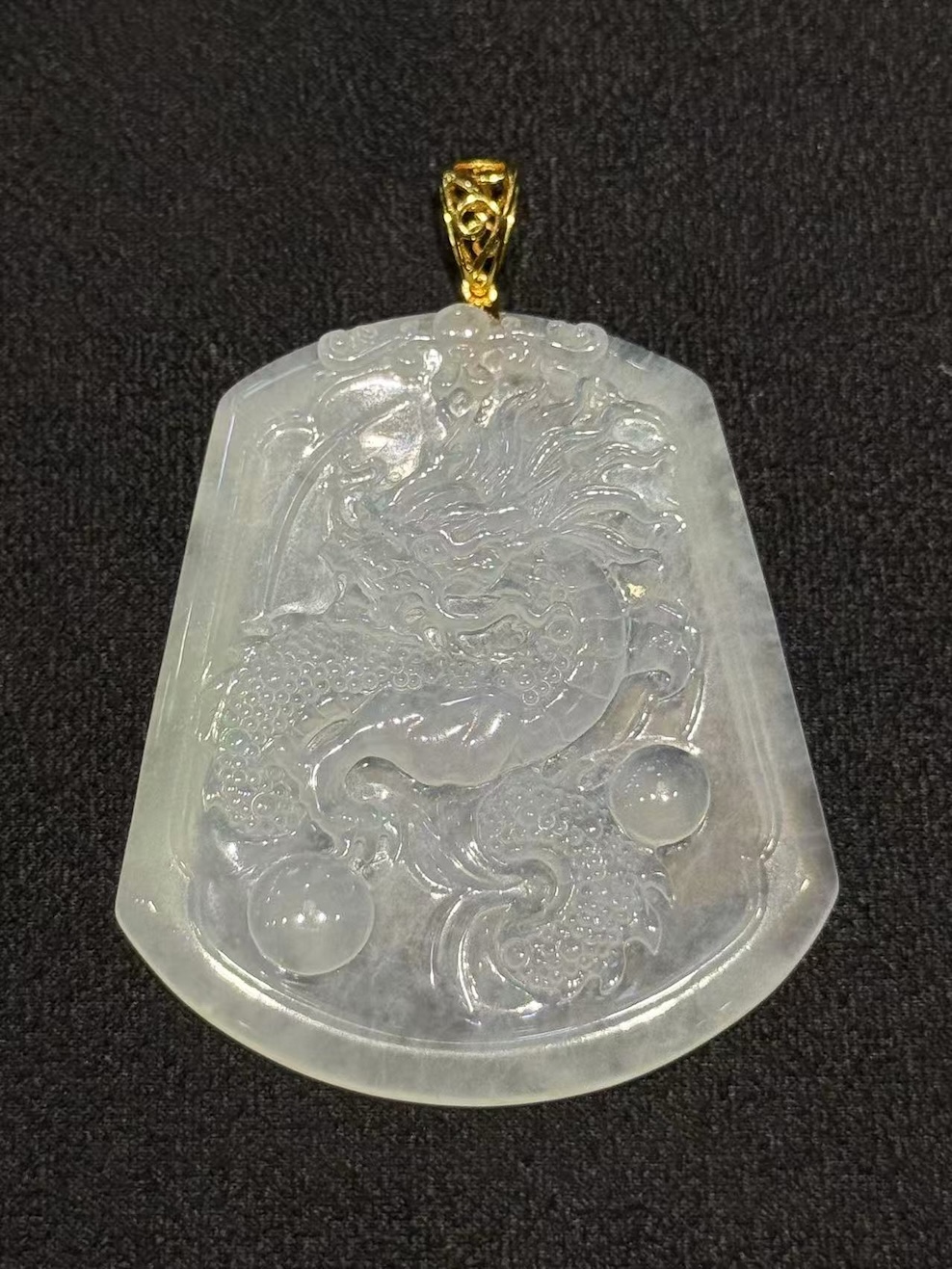 Dragon jade pendant hand-carved from icy translucent jadeite on a trapezoidal plaque, showing a dragon chasing a flaming pearl, finished with an 18k yellow gold bail