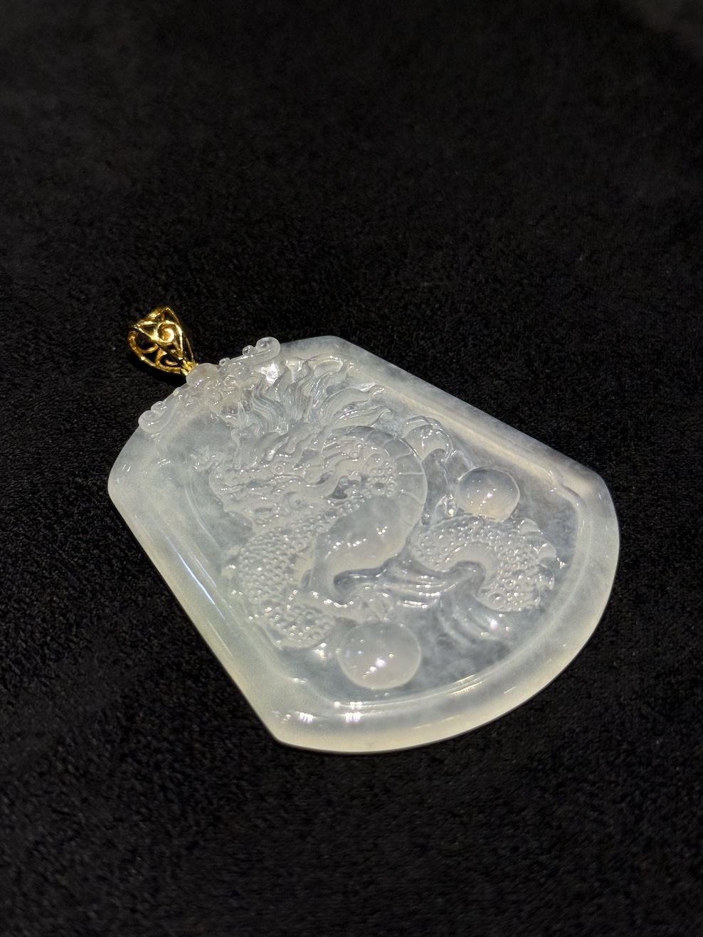 Dragon jade pendant hand-carved from icy translucent jadeite on a trapezoidal plaque, showing a dragon chasing a flaming pearl, finished with an 18k yellow gold bail