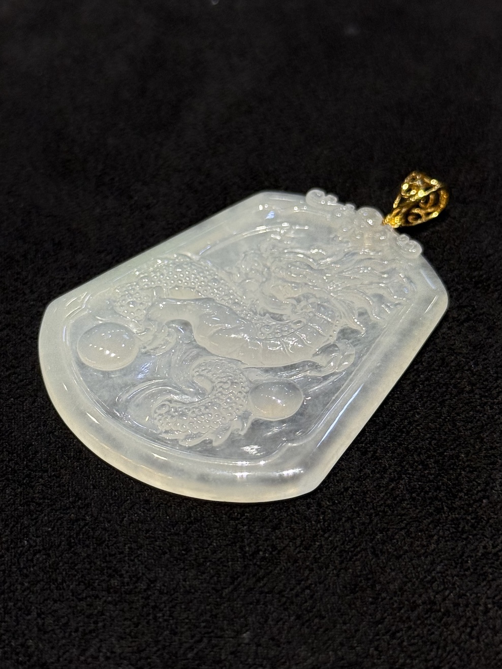 Dragon jade pendant hand-carved from icy translucent jadeite on a trapezoidal plaque, showing a dragon chasing a flaming pearl, finished with an 18k yellow gold bail