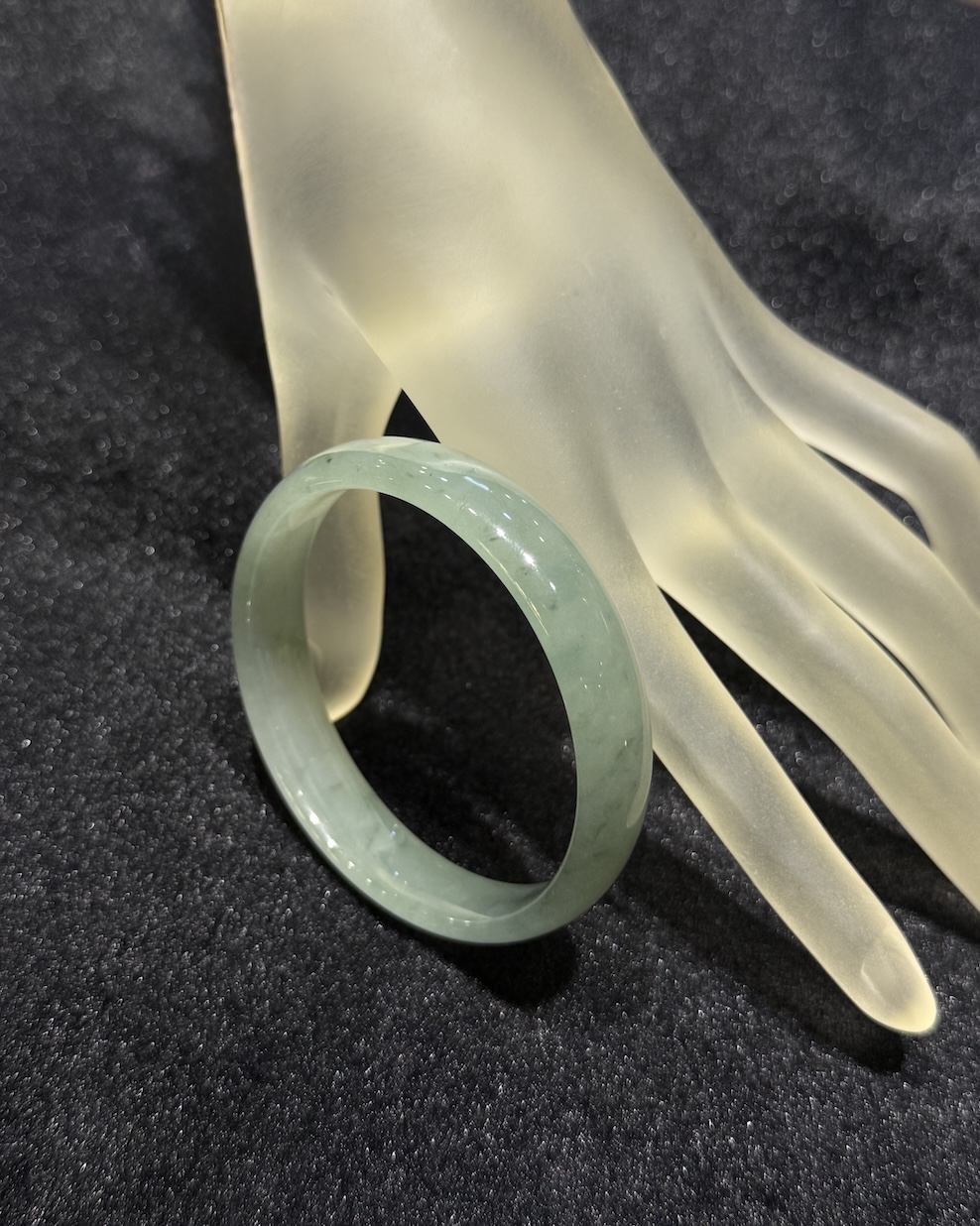 Translucent jadeite bangle in an icy, near-colourless body with a very faint green tint and small darker green flecks drifting through the ring