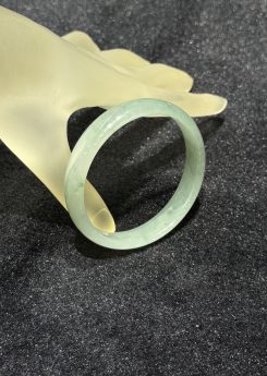 Translucent jadeite bangle in an icy, near-colourless body with a very faint green tint and small darker green flecks drifting through the ring