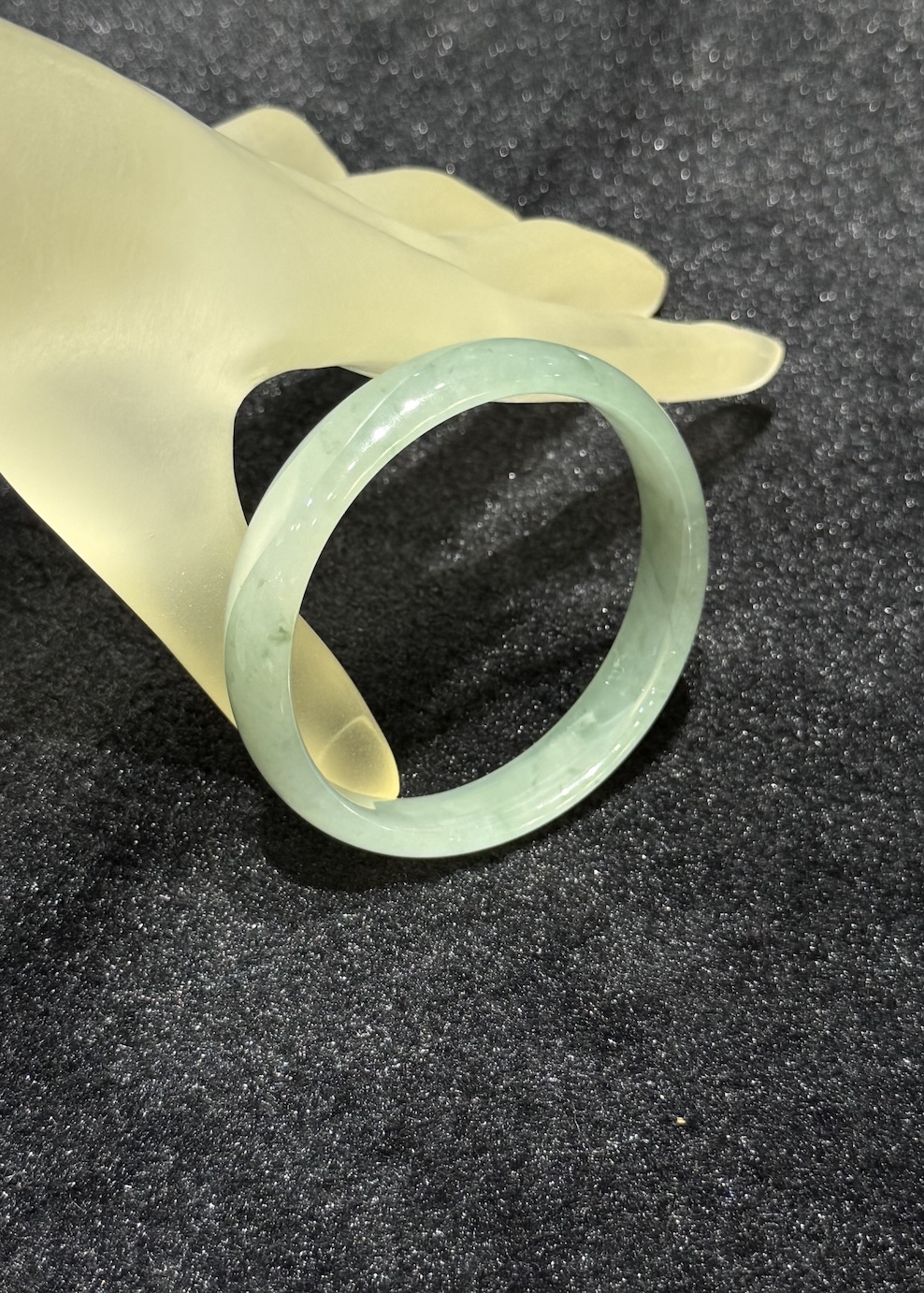 Translucent jadeite bangle in an icy, near-colourless body with a very faint green tint and small darker green flecks drifting through the ring