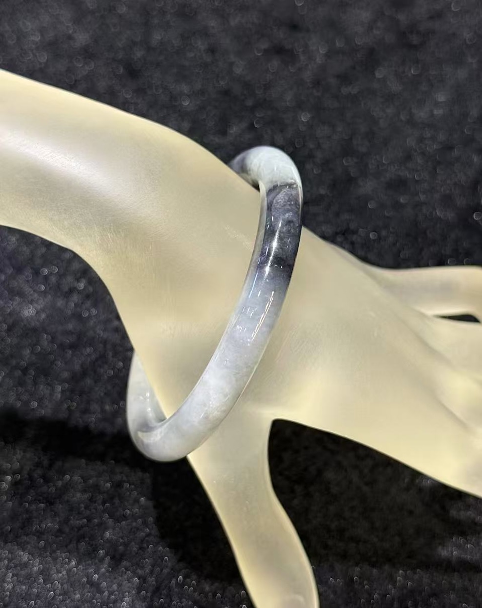Grey jade bangle in a translucent, smoky grey jadeite with darker greyish-black patches, carved in a round cut from a single piece of jade