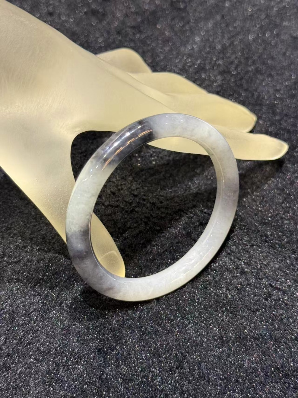 Grey jade bangle in a translucent, smoky grey jadeite with darker greyish-black patches, carved in a round cut from a single piece of jade
