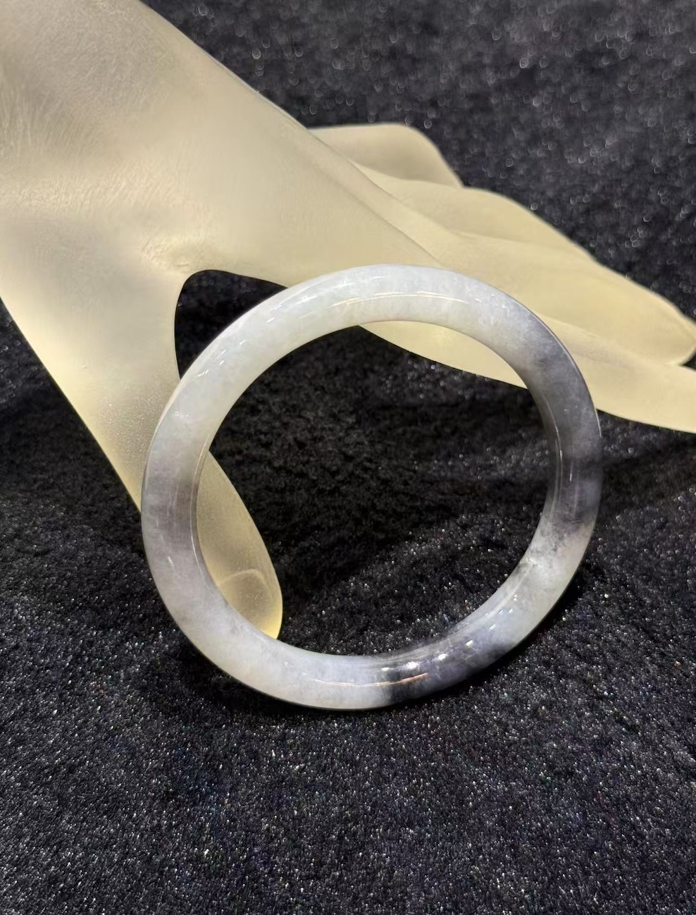 Grey jade bangle in a translucent, smoky grey jadeite with darker greyish-black patches, carved in a round cut from a single piece of jade
