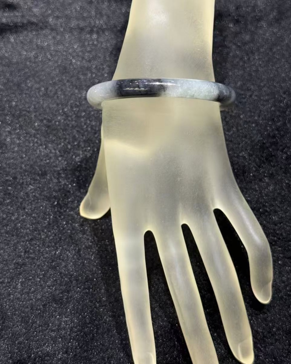 Grey jade bangle in a translucent, smoky grey jadeite with darker greyish-black patches, carved in a round cut from a single piece of jade