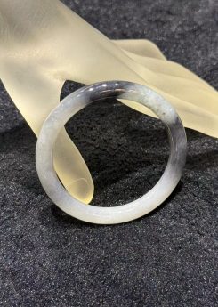 Grey jade bangle in a translucent, smoky grey jadeite with darker greyish-black patches, carved in a round cut from a single piece of jade