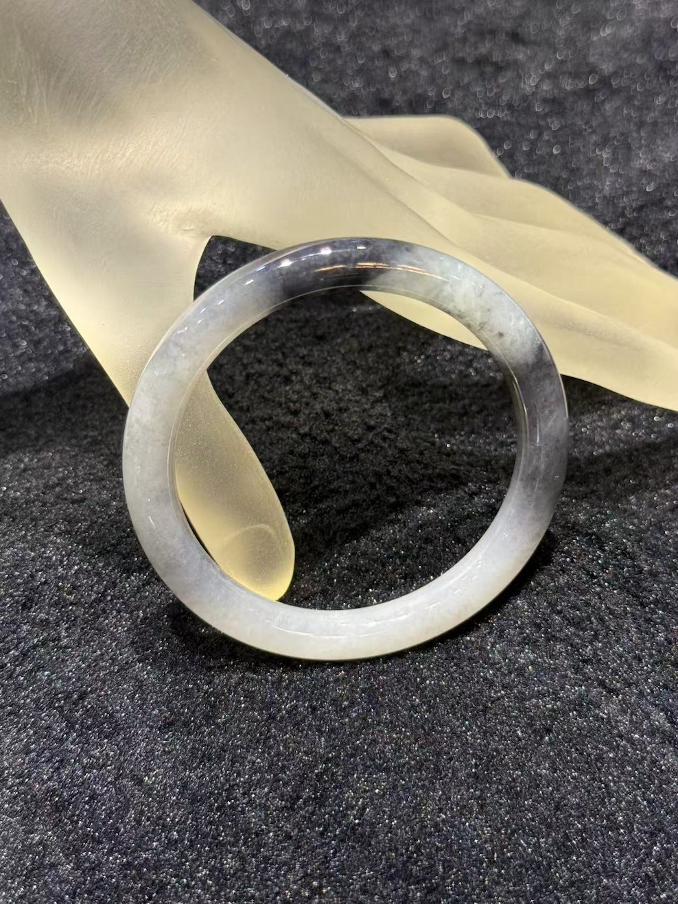 Grey jade bangle in a translucent, smoky grey jadeite with darker greyish-black patches, carved in a round cut from a single piece of jade