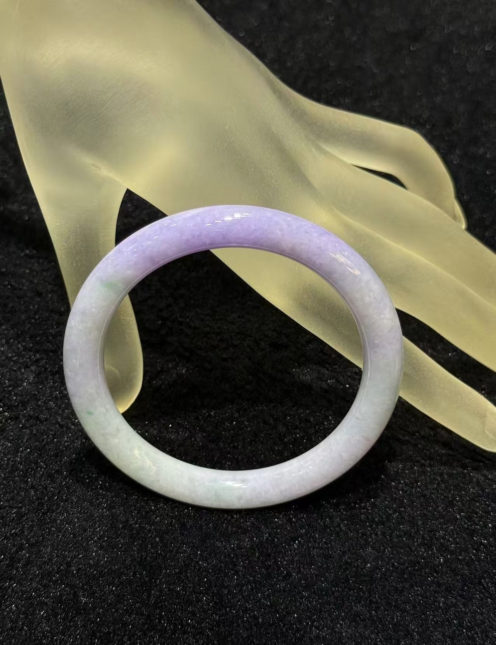 Lavender jade bangle in a translucent lavender body with faint green patches drifting through the ring, carved in a round cut