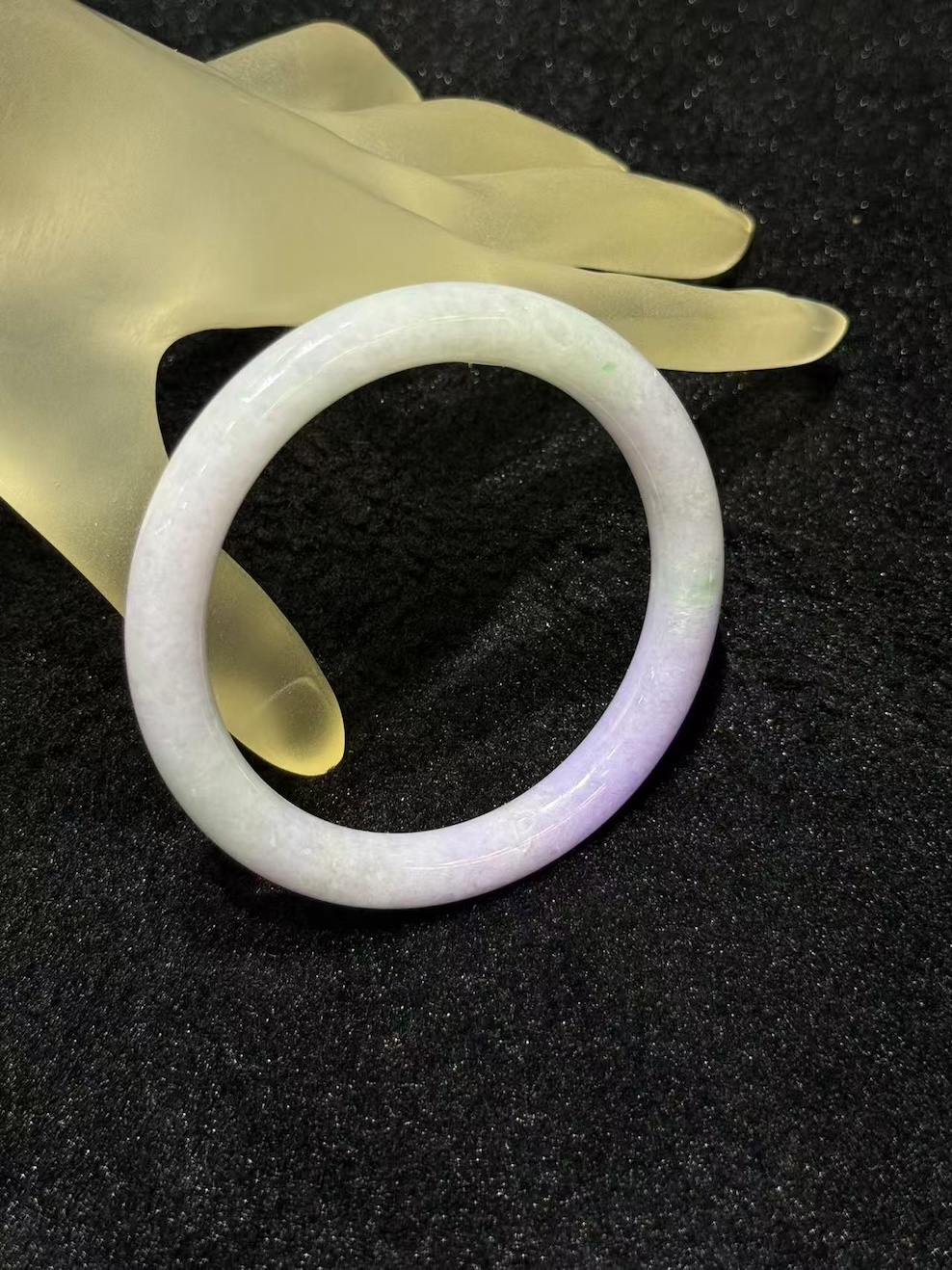 Lavender jade bangle in a translucent lavender body with faint green patches drifting through the ring, carved in a round cut