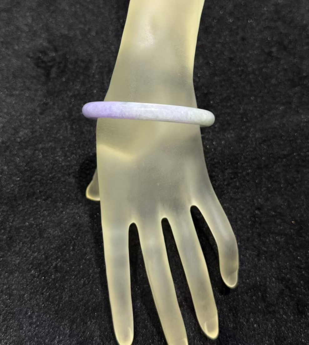 Lavender jade bangle in a translucent lavender body with faint green patches drifting through the ring, carved in a round cut