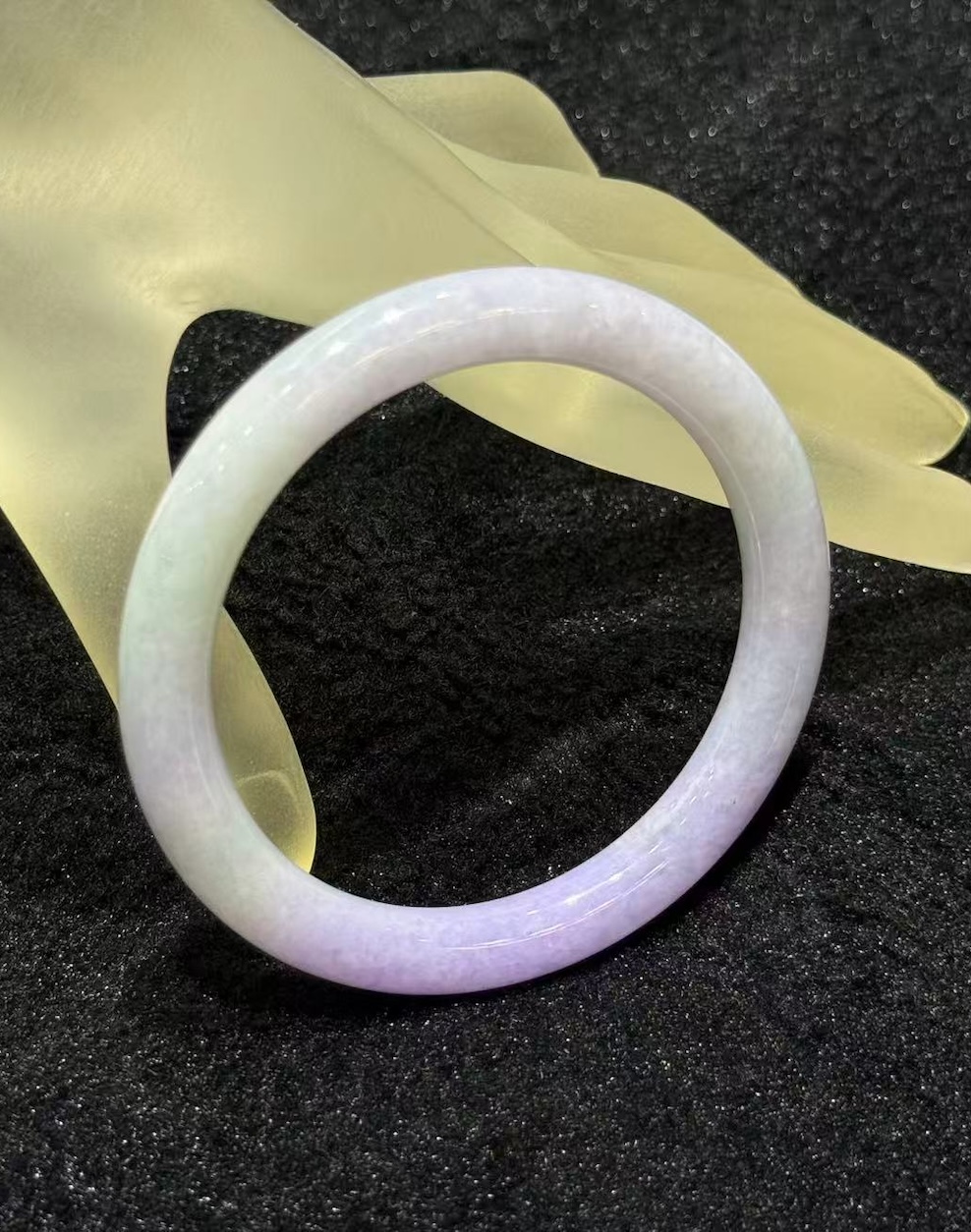 Lavender jade bangle in a translucent lavender body with faint green patches drifting through the ring, carved in a round cut