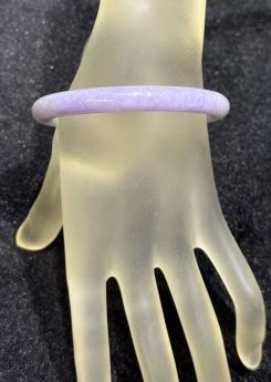 Lavender jade bangle in a translucent lavender body with faint green patches drifting through the ring, carved in a round cut