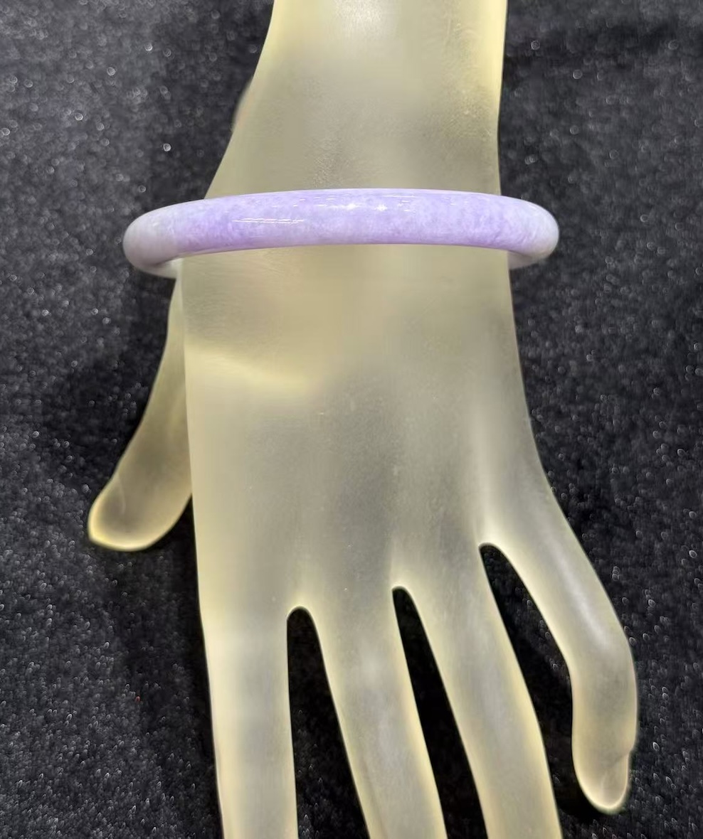 Lavender jade bangle in a translucent lavender body with faint green patches drifting through the ring, carved in a round cut